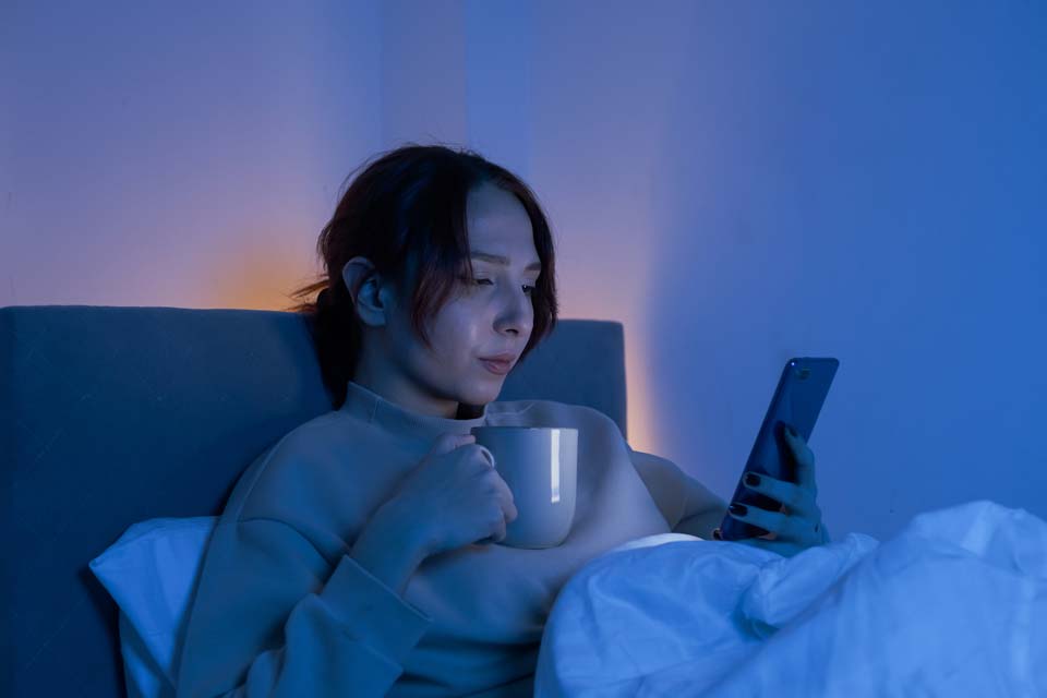 Woman sick in bed with coffee and looking at phone