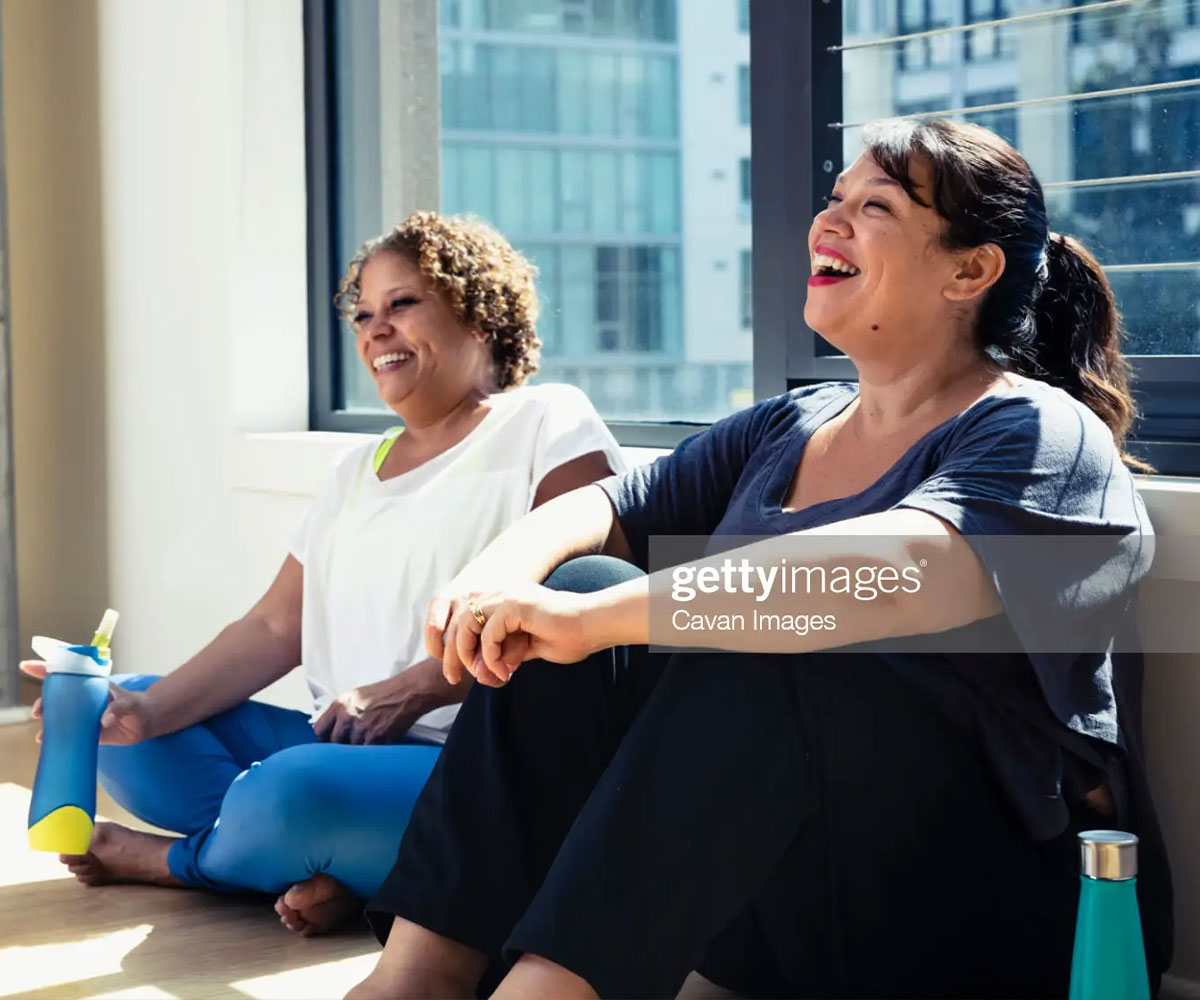 Two mature women sit on the floor after exercise class